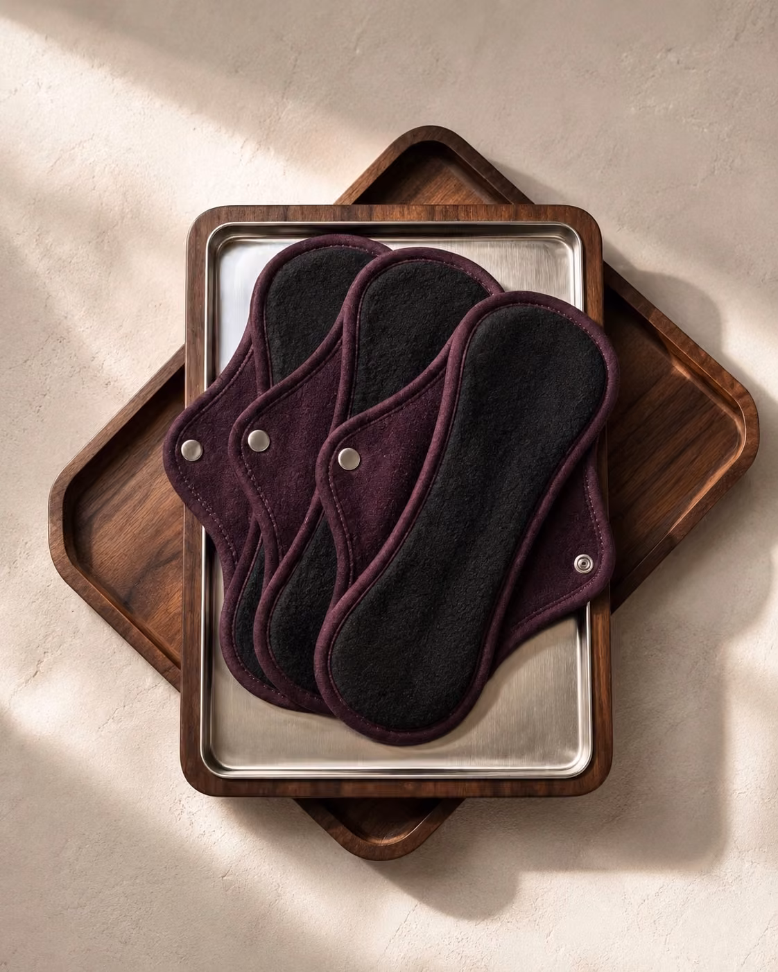 Trois protections hygiéniques amovibles bordeaux et noires présentées sur des plateaux.